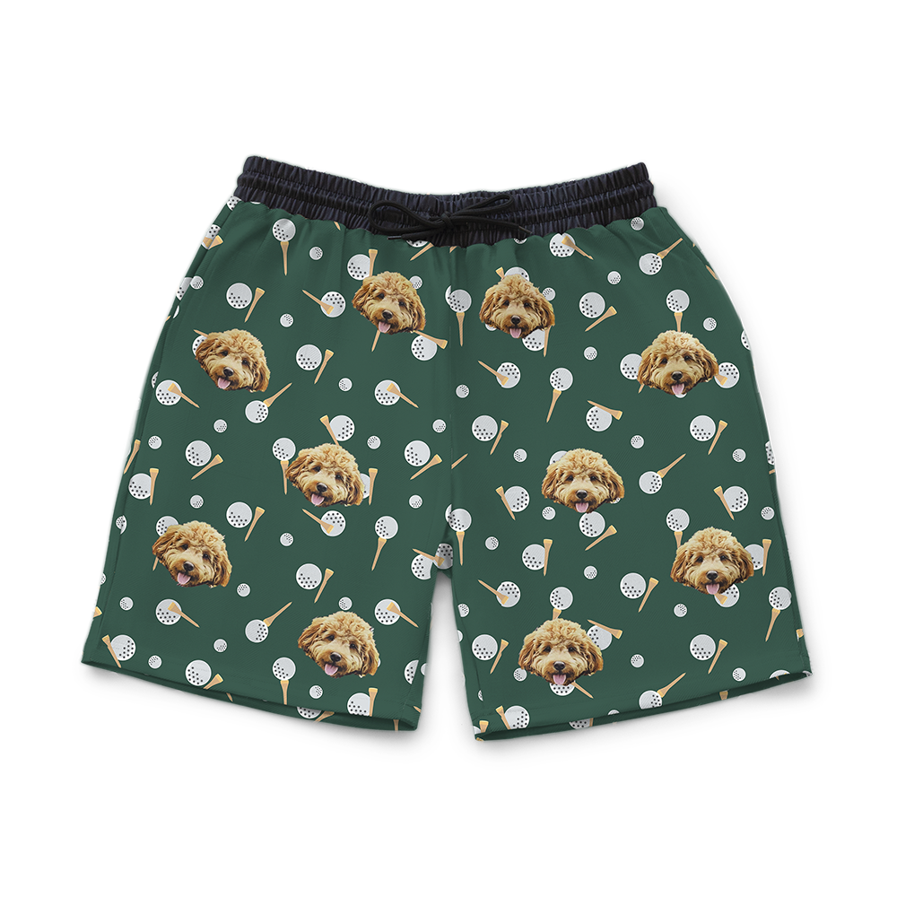 Green men’s shorts featuring a repeating pattern of a fluffy light-brown dog’s face along with scattered golf balls and golf tees.