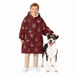 A young boy wearing a long burgundy hooded sweatshirt with a dog print pattern, standing next to a black and white dog on a solid white background.