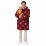 A man wearing a burgundy hooded fleece blanket robe with a Gryffindor cat pattern, holding an orange tabby cat, standing against a white background.