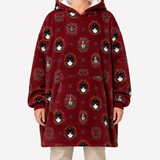 A person wearing a burgundy hooded sweatshirt with an all-over print of black-and-white cat portraits in ornate circular frames, paired with light beige pants, against a plain light gray studio background.
