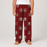A person wearing red pajama pants with a repeating print of Dalmatian dog faces and circular portrait medallions, shown from the waist down against a light gray studio background.