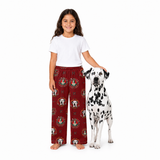 A young girl stands barefoot next to a Dalmatian dog on a white studio background, wearing a white T-shirt and burgundy pajama pants with a repeating firefighter helmet and badge print.