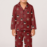 A child wearing a matching long-sleeve pajama set in burgundy red with an all-over print of black cats in ornate circular frames, photographed against a plain light gray studio background.