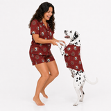 A woman and a Dalmatian dog wearing matching burgundy pajama sets with a dog-themed print, posing together against a white studio background.