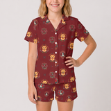 A woman modeling a matching short-sleeve button-front pajama shirt and shorts set in burgundy with a repeating golden retriever and crest pattern, against a light gray studio background.