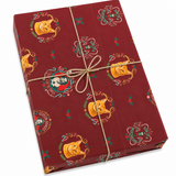 A rectangular gift box wrapped in dark red Halloween-themed paper with orange jack-o'-lanterns, green holly accents, and decorative scrollwork, tied with a natural twine bow on a white background.
