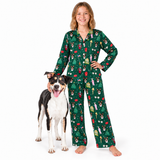 A woman wearing a green long-sleeve pajama set with a Christmas-themed dog print stands barefoot next to a black, white, and tan dog on a solid white background.