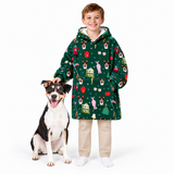 A young boy wearing a green Christmas-themed fleece hoodie with a dog sitting next to him, photographed against a solid white studio background.