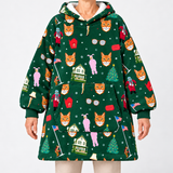 A person wearing a dark green hooded pullover sweatshirt with an all-over festive print of fox faces, Christmas houses, trees, flags, and holiday figures. The image is cropped from the neck down against a plain light gray studio background.