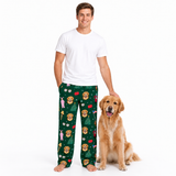 A man wearing dark green Christmas-themed pajama pants with a lion print stands next to a golden retriever dog on a white studio background. The man is also wearing a plain white t-shirt.