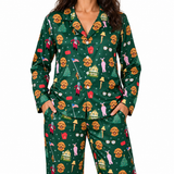 A woman wearing a matching long-sleeve pajama set with a dark green Christmas-themed print featuring golden retriever dogs, Santa Claus, Christmas trees, houses, and snowflakes. The top has a buttoned collar, and the pants have front pockets.