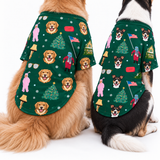 Two dogs wearing matching green Christmas-themed dog shirts with a festive print of golden retriever faces, Christmas trees, snowflakes, and holiday figures, photographed against a clean white background.