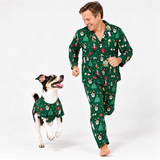 A man and a dog wearing matching green Christmas-themed pajamas with a festive print of Santa Claus, snow globes, and Christmas trees, posed against a clean white studio background.
