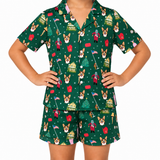 A child wearing a matching green short-sleeve pajama top and shorts set with a festive Christmas dog print, posed against a plain white background.