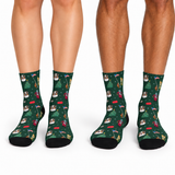 Three pairs of crew socks worn on legs, featuring a dark green Christmas-themed print with dogs, trees, flags, and holiday motifs on a white background.