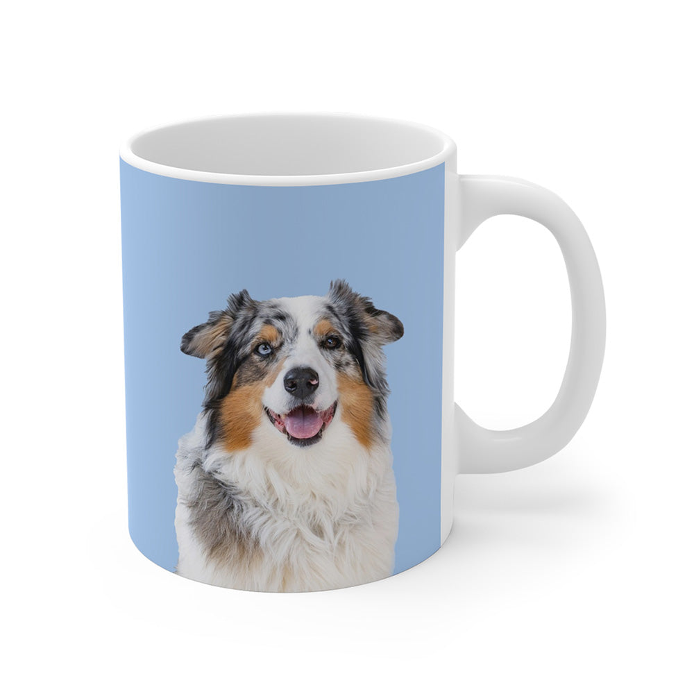 A clean product shot of a blue ceramic mug featuring a smiling, multicolored Australian Shepherd