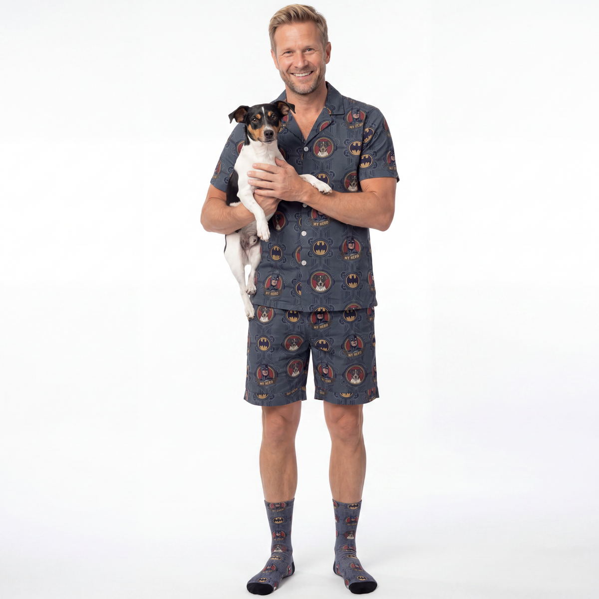 Man wearing a batman pajama set holding a small dog on a white background