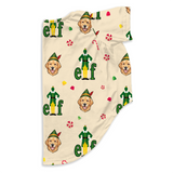 A cream-colored blanket featuring a repeating pattern of golden retriever dog faces and green and yellow elf figures, with small candy cane and confetti accents.