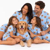 A family of four and their golden retriever dog wearing matching light blue pajamas printed with a repeating dog face pattern, posed together on a white studio background.