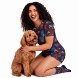 A woman kneeling on a white studio background, hugging a brown poodle. She is wearing a Supergirl-themed short-sleeve fitted shirt set and matching socks with a repeating dog prints and supergirl logo.