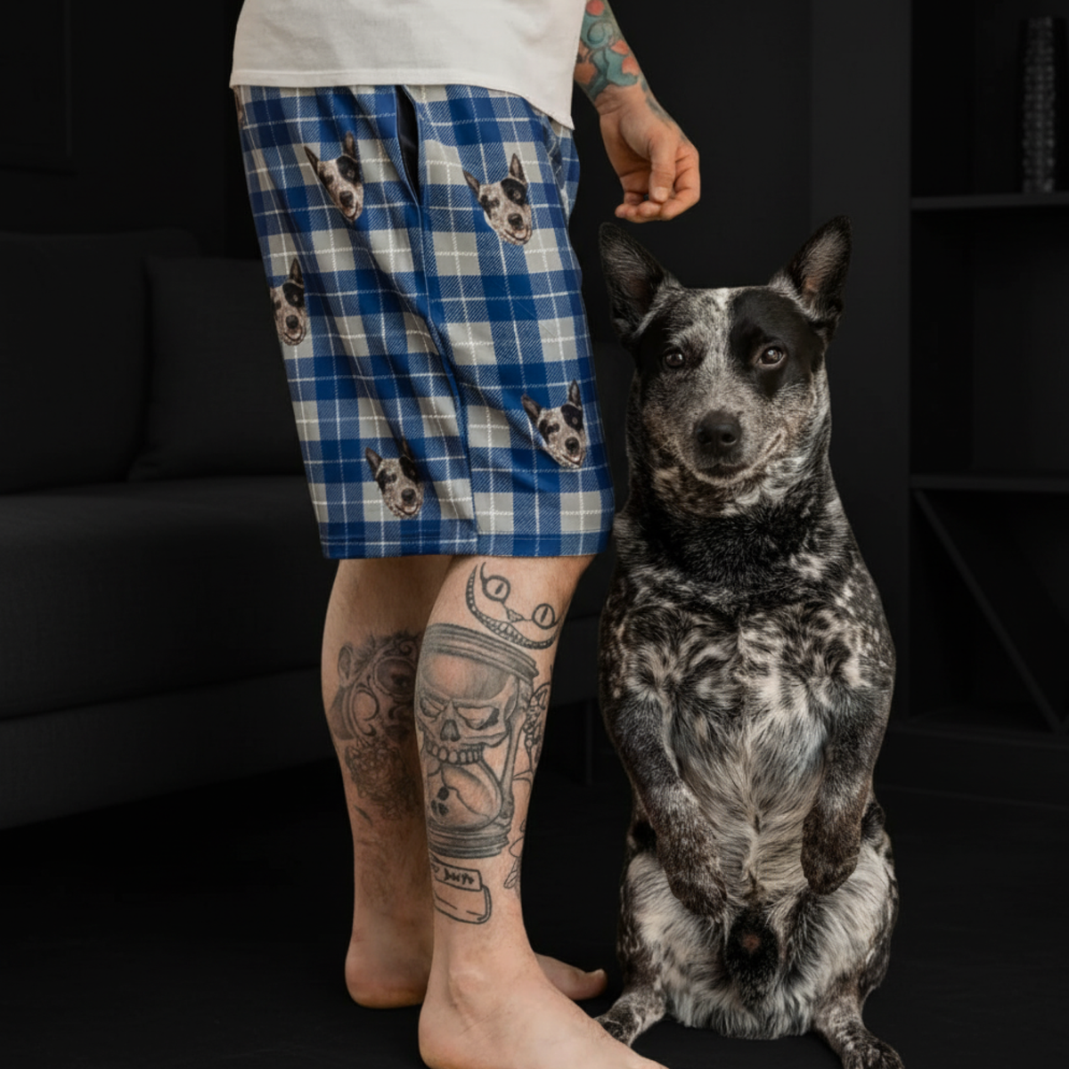 Person wearing blue plaid shorts with dog prints, standing next to a black and white dog indoors.