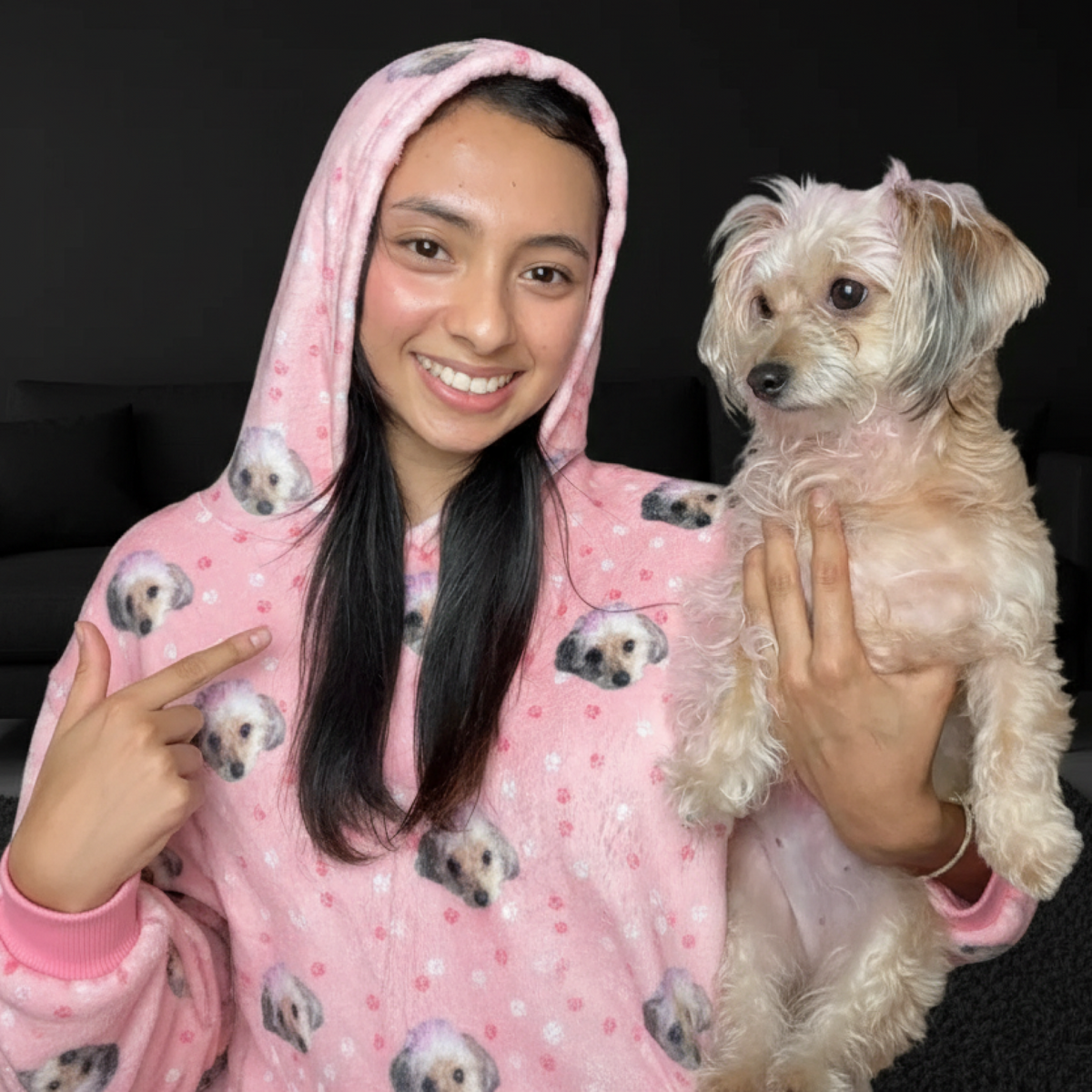 Person wearing a pink hoodie with dog patterns, holding a small dog.