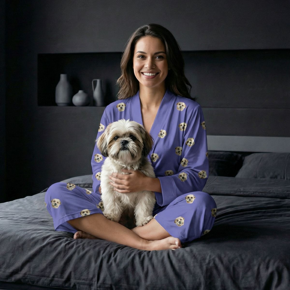 Woman in purple pajamas with skull patterns holding a small dog on a bed.