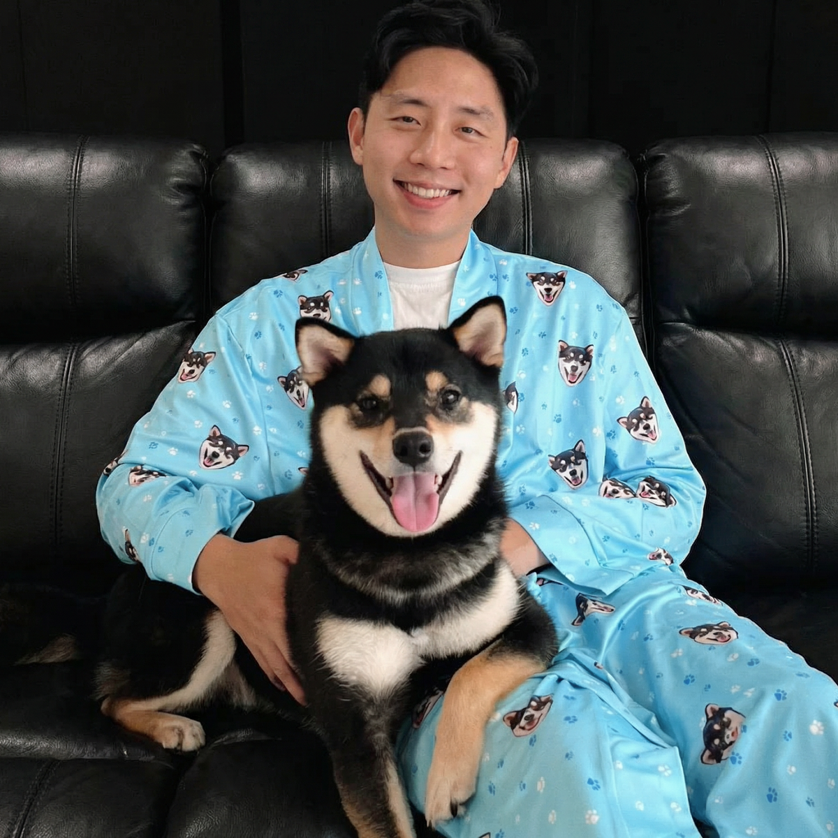 Man in a blue robe with dog patterns sitting on a couch with his dog.