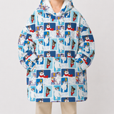 A person wearing a hooded oversized jacket with an all-over repeating print of cartoon dogs in winter outfits on a light blue and white background, paired with light beige pants, against a plain light gray studio backdrop.