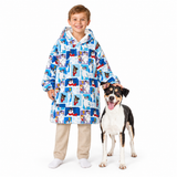 A smiling young boy wearing a hooded sweatshirt-style poncho with a colorful cartoon dog print, standing next to a black, white, and tan dog on a plain white studio background.