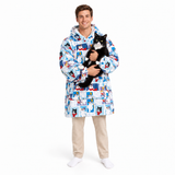 A man wearing a hooded long coat with a colorful cartoon cat print, holding a black and white cat against his chest, standing on a white studio background.
