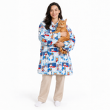 A woman wearing a light blue hooded robe with a cartoon patchwork print holds an orange tabby cat against a plain white studio background.