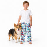 A young boy wearing a white t-shirt and blue patterned pajama pants stands next to a corgi dog on a seamless white background.