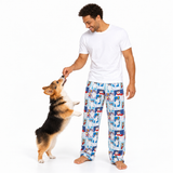 A man wearing a white t-shirt and blue patterned pajama pants plays with a corgi dog on a white studio background.