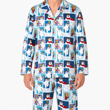 A man wearing a matching long-sleeve pajama shirt and pants set with a repeating cartoon dog print on a light blue background, photographed against a plain light gray studio backdrop.