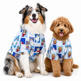 Two dogs wearing matching blue patterned pet shirts with cartoon penguin illustrations, photographed against a clean white studio background.