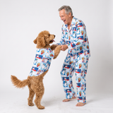 A man and his dog wearing matching blue and white cartoon-print pajamas, standing and playing against a plain white studio background.