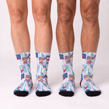 Three pairs of crew socks with a colorful cartoon collage print, worn on legs against a plain white studio background.