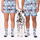 A Dalmatian stands between two cropped human models wearing matching shorts and socks with a repeating cartoon dog print on a white studio background.