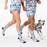Two people jogging while wearing matching shorts and socks with a colorful cartoon dog print, alongside a Dalmatian dog on a white studio background.