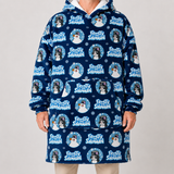 A person wearing a navy hooded sweatshirt with an allover 'Frosty Snowman' print, featuring penguin illustrations and white text, paired with light beige pants against a light gray studio background.