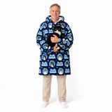 An older man wearing a navy blue hooded robe with a white and light blue 'Just Chill' cat print pattern, holding a black and white cat against his chest. He is wearing beige pants and white socks, standing against a solid white studio background.