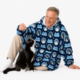 A smiling older man sits on a white studio floor wearing a navy hooded sweatshirt covered in a repeating 'Food99 Smart Dog' dog-themed print, with beige pants and white socks. A black-and-white cat sits beside him.