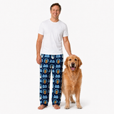 A man wearing blue patterned pajama pants and a plain white t-shirt stands barefoot next to a golden retriever dog on a clean white background.