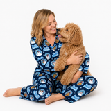 A woman wearing blue pajamas with a cartoon dog pattern sits on the floor, smiling and hugging a fluffy golden-brown dog against a plain white background.