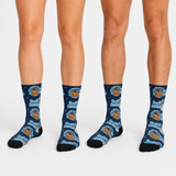 Three lower legs wearing matching crew socks with a dark blue background and a repeating cartoon dog face pattern in light blue, tan, and white. The socks are shown on a plain light gray studio background.