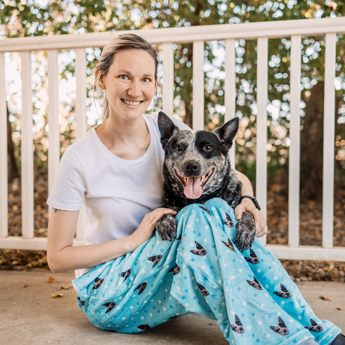 Woman wearing sky blue dog-print pajama pants sitting on a porch with a black and gray dog.