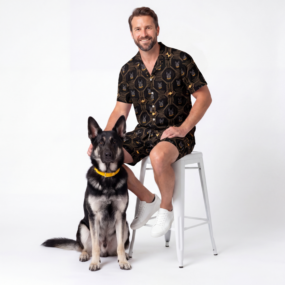 Man sitting on a stool with a dog wearing batman pajama against a white background