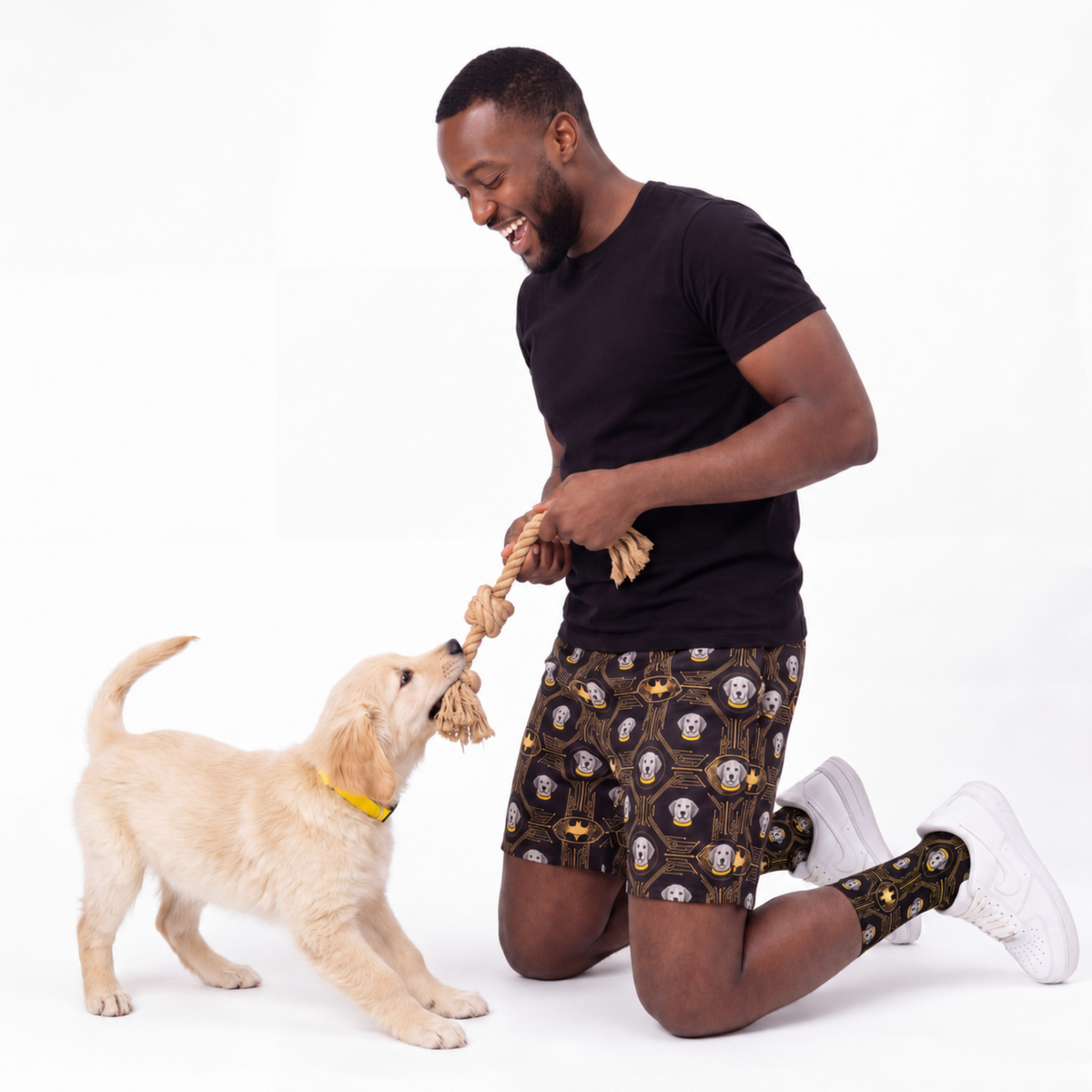 Man wearing batman shorts playing with a puppy on a white background