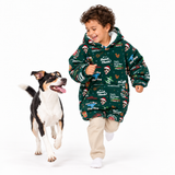 A child running while wearing a green Christmas-themed hooded sweatshirt with a dog beside them, photographed on a clean white studio background.